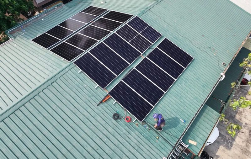Aerial view of the finished panel array on a green corrugated roof, one installer finishing the cabling.